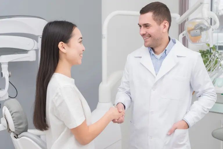 Un médecin-dentiste accueille une patiente avec une poignée de main souriante