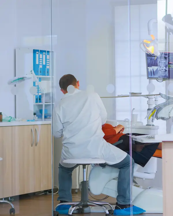 Un médecin-dentiste en consultation, vu depuis l’accueil vitré du cabinet